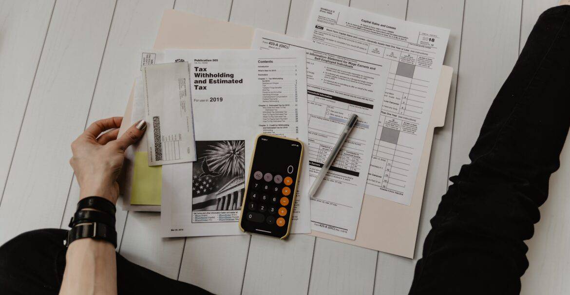 person holding paper near pen and calculator