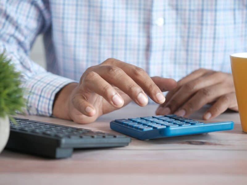 person using calculator at desk with coffee mug